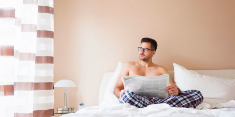 Young man sat in bed with newspaper gazing out the window