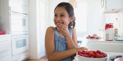 Smiling girl eating fresh berries in kitchen