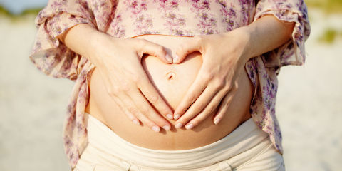 Pregnant woman making heart shape on stomach with hands